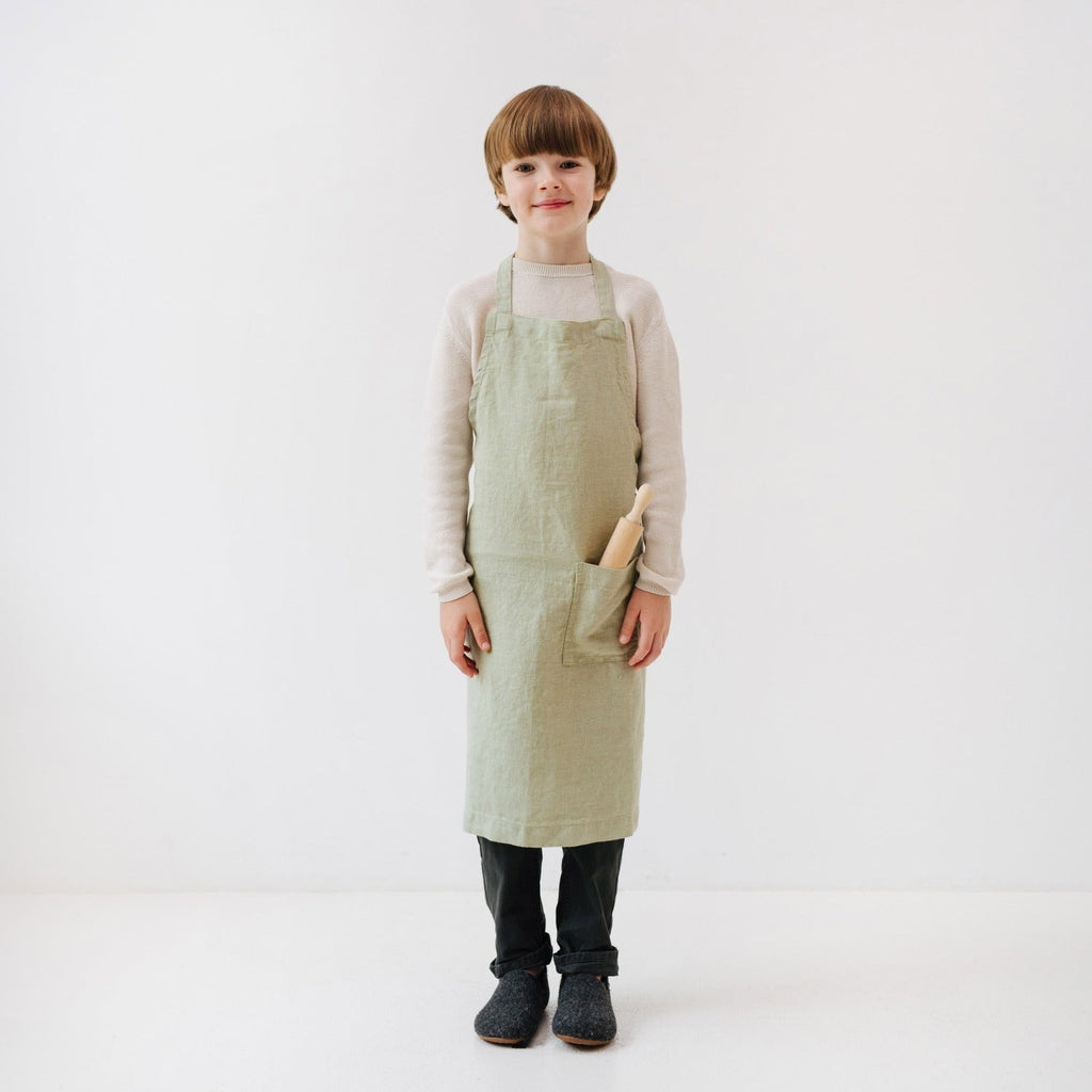 side view of a child's sage linen apron showing the adjustable tie closure and deep front pocket