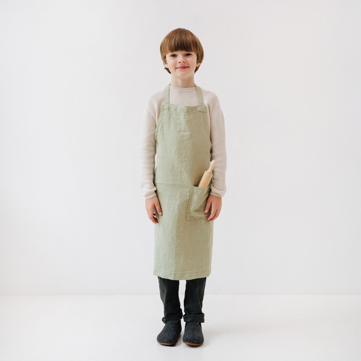 side view of a child's sage linen apron showing the adjustable tie closure and deep front pocket