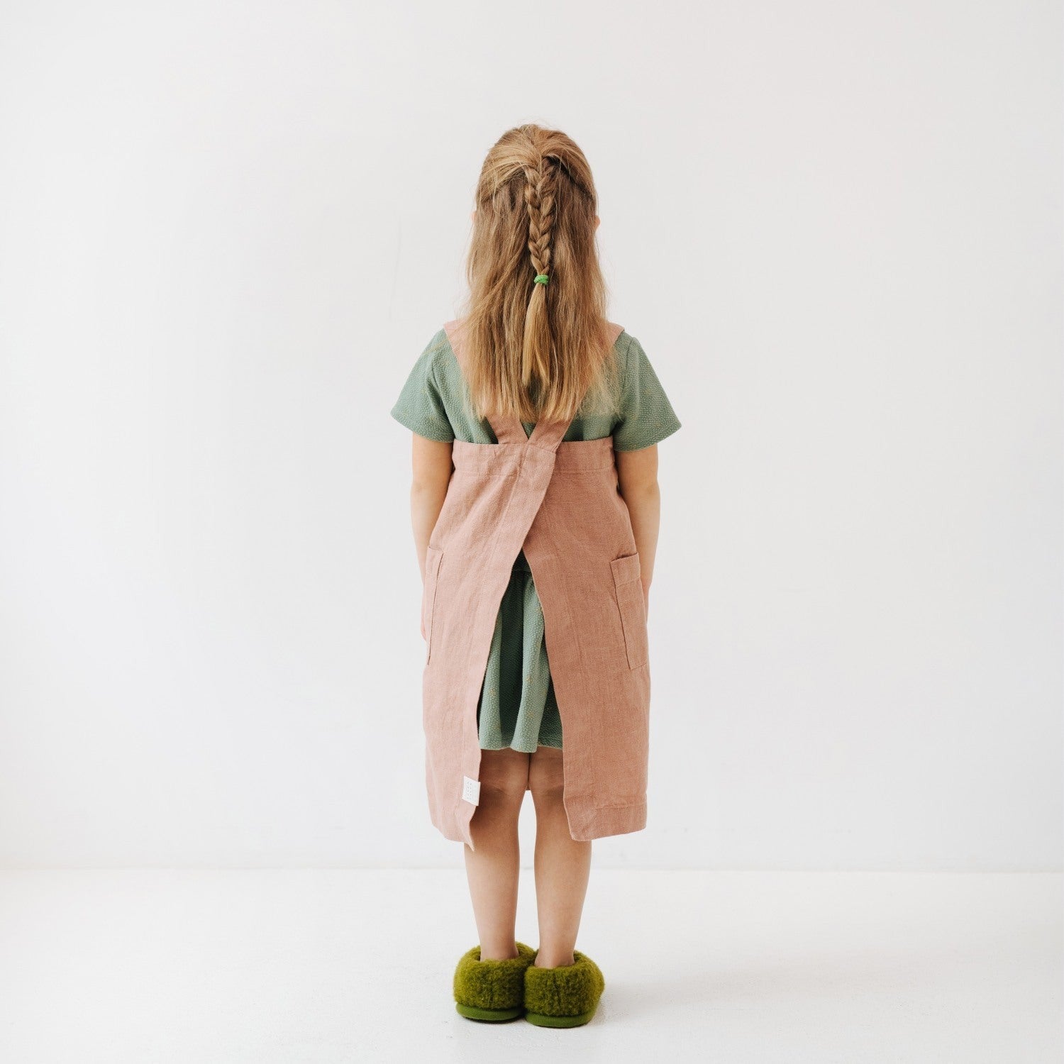 a soft linen pinafore apron for kids in cafe creme, shown in gentle morning light with two deep front pockets for tools