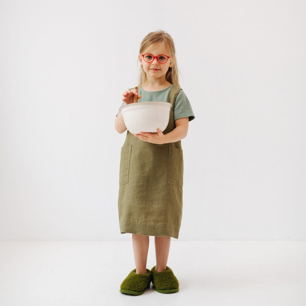 soft olive linen kids apron with two pockets, shown in gentle morning light