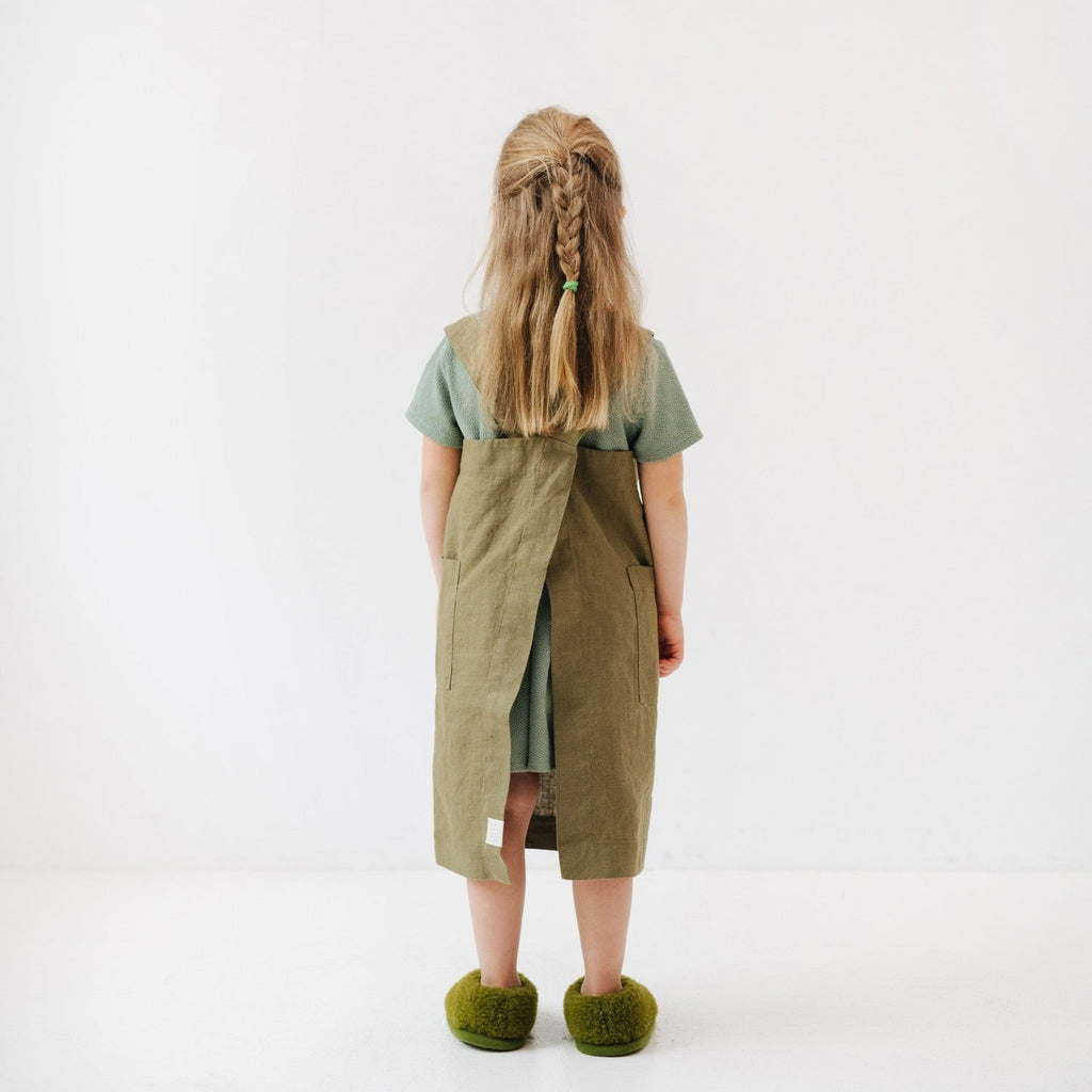 a child laughing while wearing an olive linen pinafore apron, ready for a playful kitchen adventure