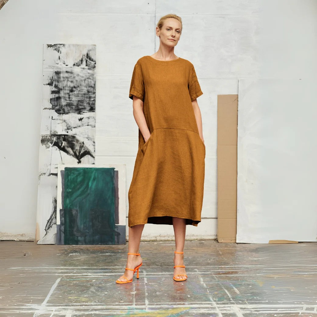 confident woman in a bronze linen a-line dress with front pockets, standing boldly against a minimalist backdrop