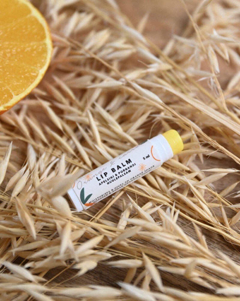 orange and carrot lip balm glowing with a playful citrus splash on a sunny yellow background