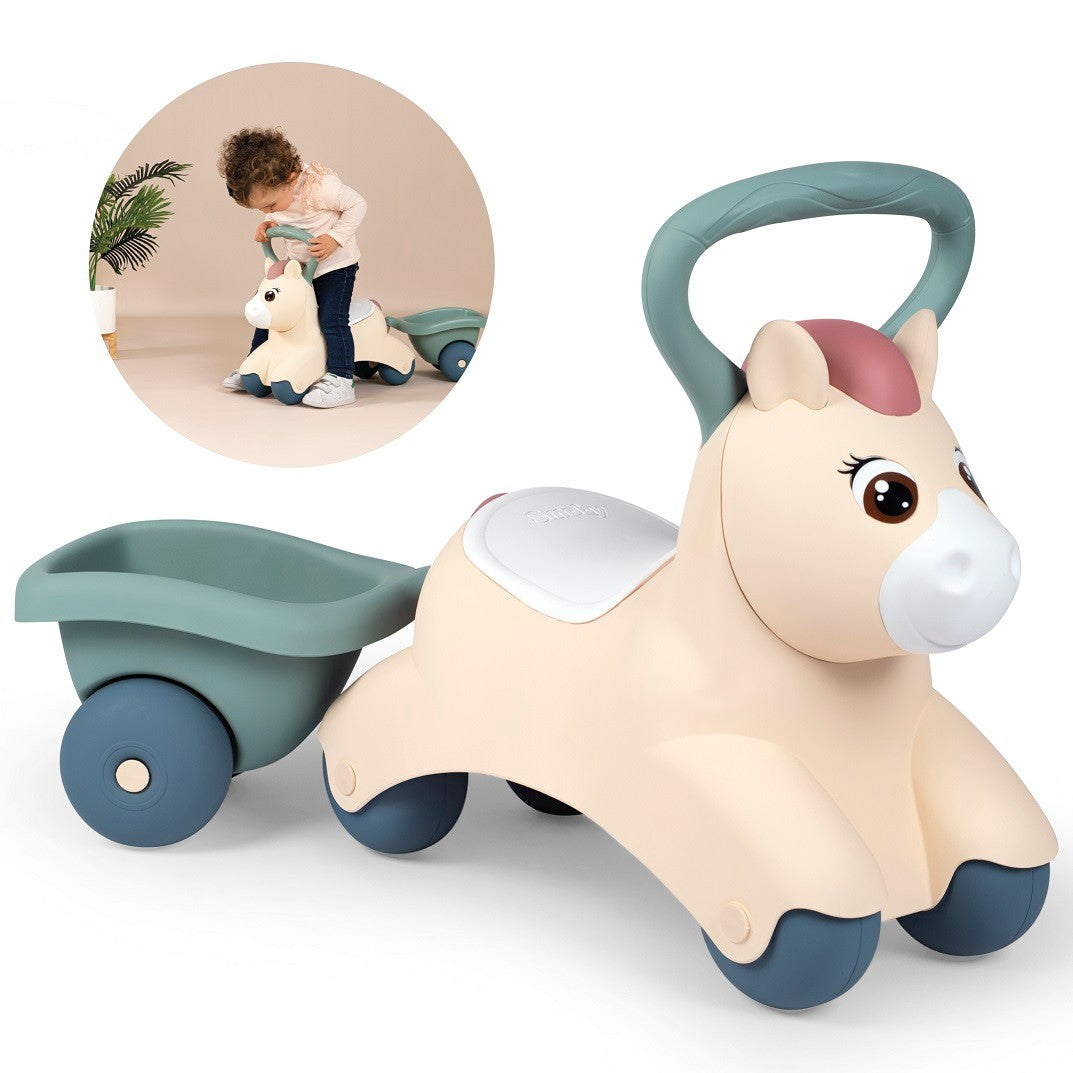 a toddler testing the sturdy handle and practical 21cm seat height of a pastel ride-on pony with trailer
