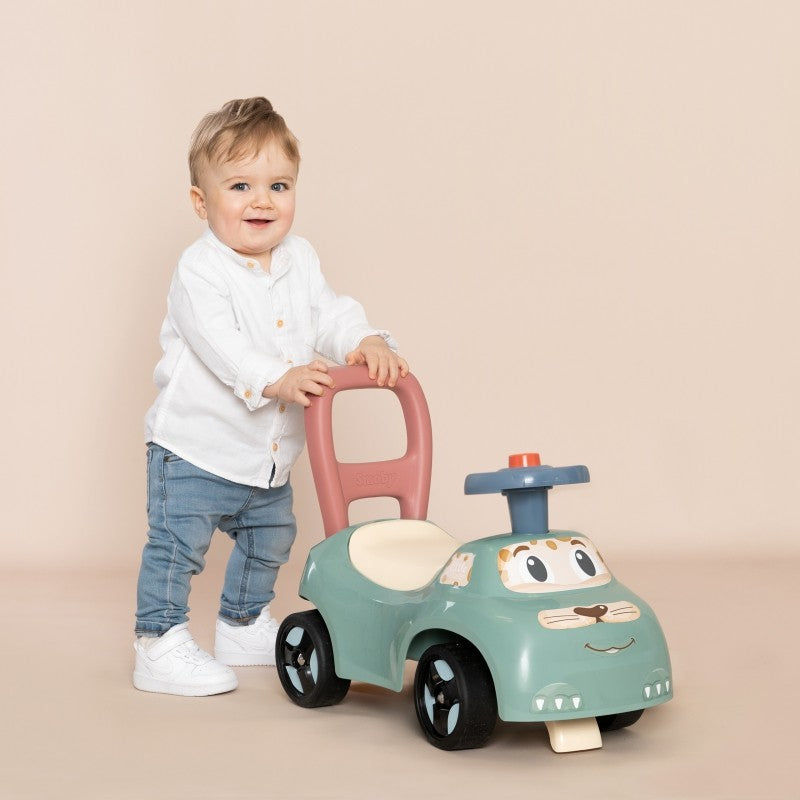 soft pastel ride-on pusher with horn, toddler pushing it on a sunny patio, learning to walk