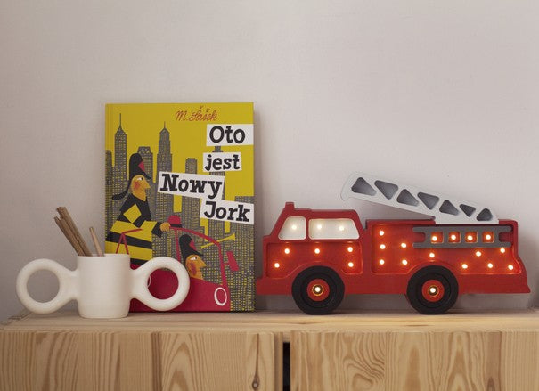 bold little lights firetruck lamp glowing warmly on a dark wood surface