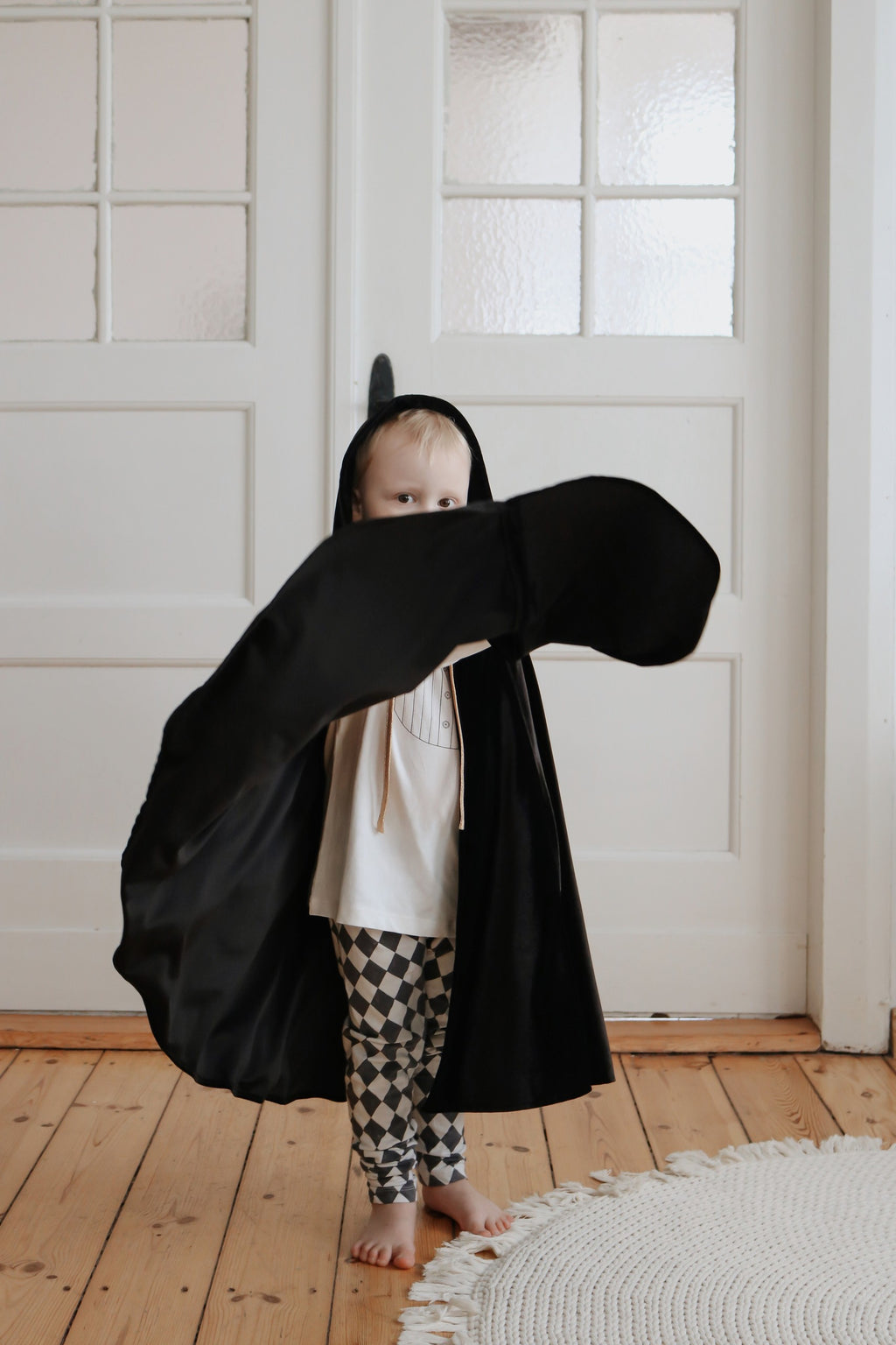 a young sorceress in a black velour cape, hands through the holes, ready for a magical quest
