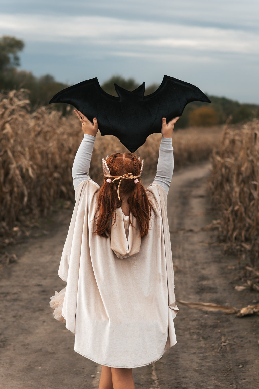 child in cream pearl magic cape with hood up, playing in a sunlit garden
