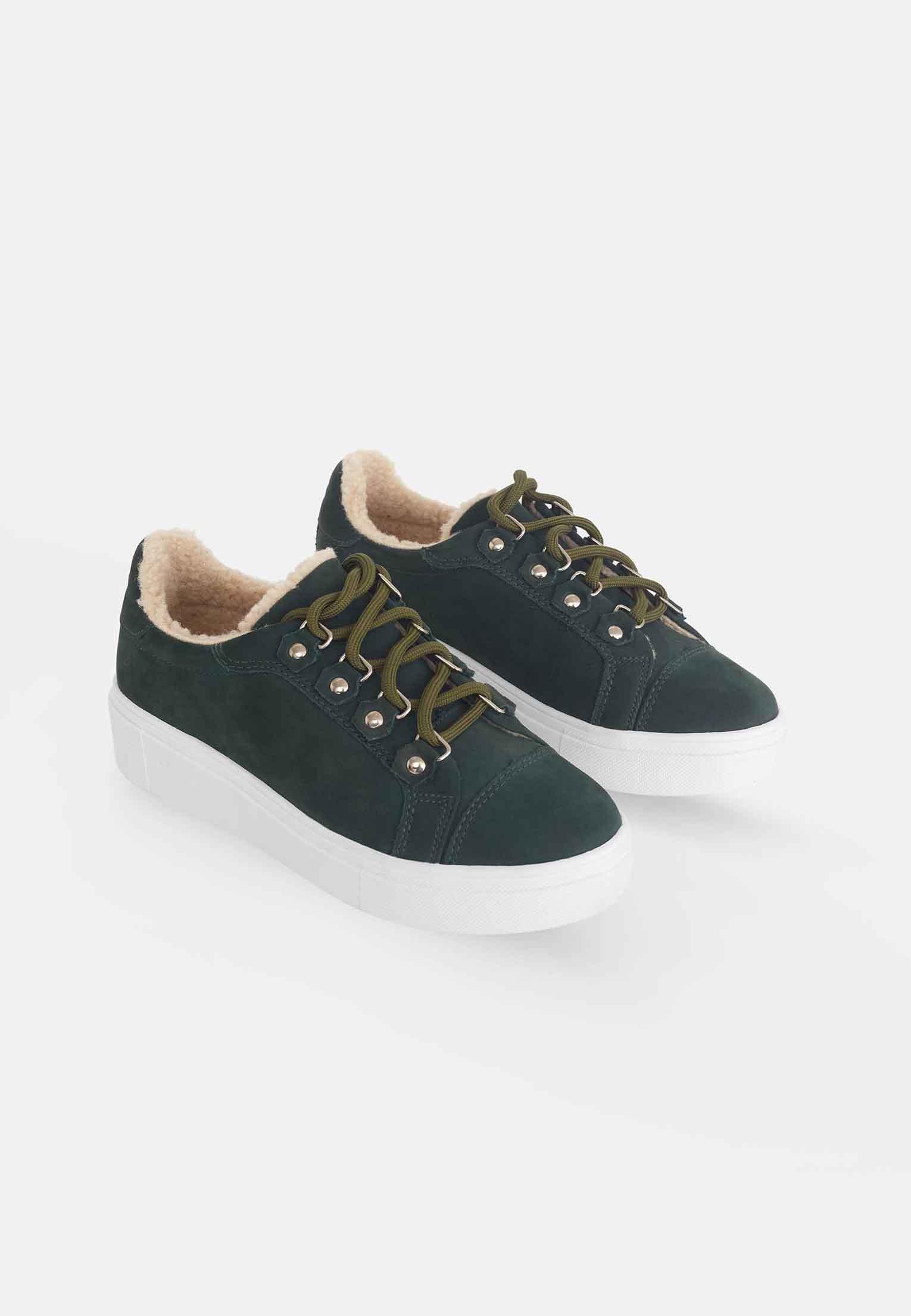 side profile of green suede winter sneakers on a textured surface, highlighting the durable rubber sole and practical platform