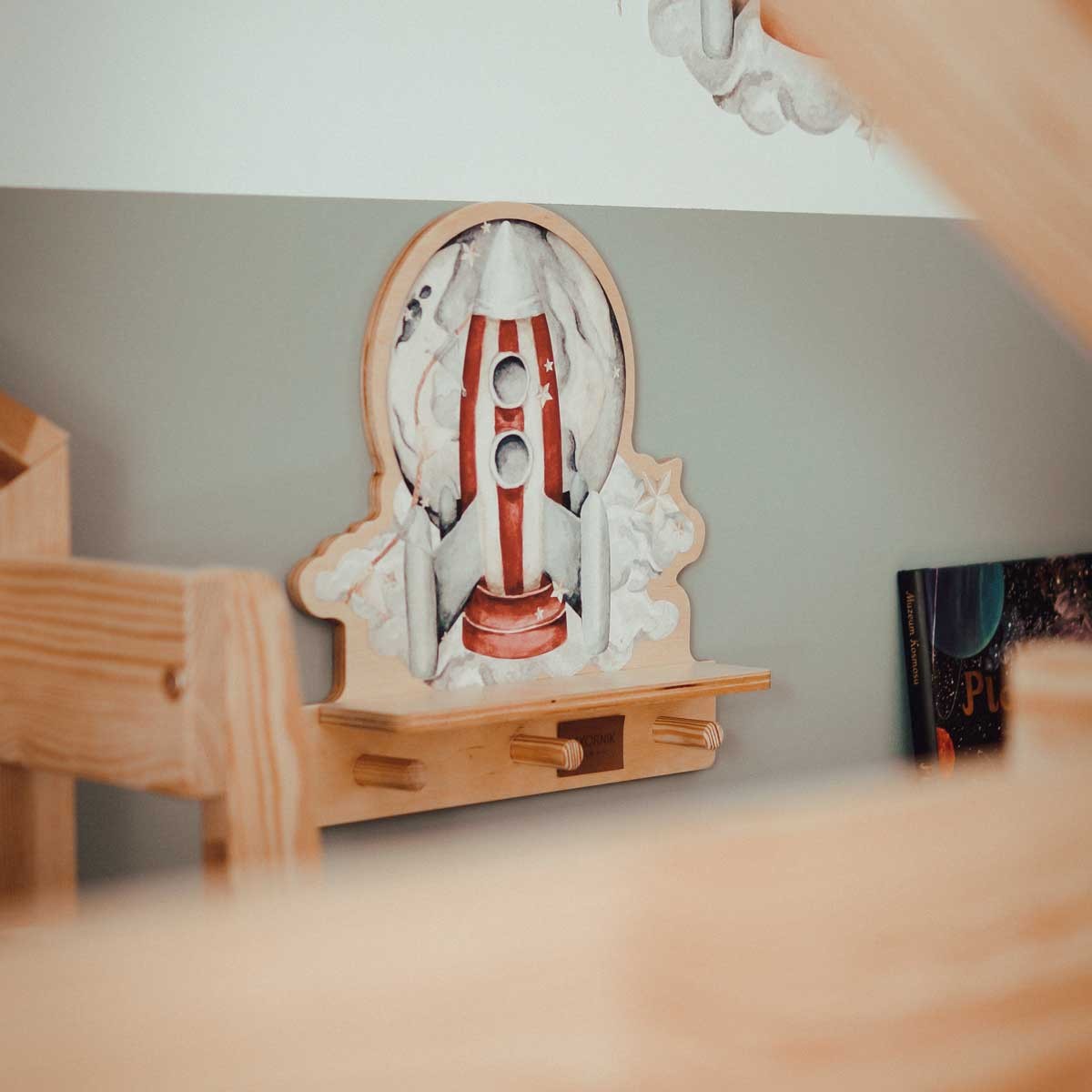 a playful rocketship wall shelf with a dinosaur sticker and three pegs for hanging small items
