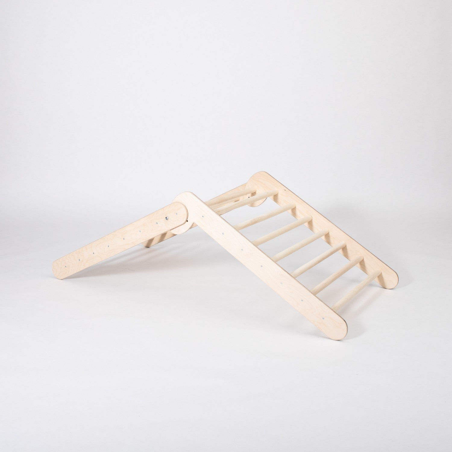 montessori climbing triangle in a sunlit playroom, toddler gripping the sturdy birch rungs with determination