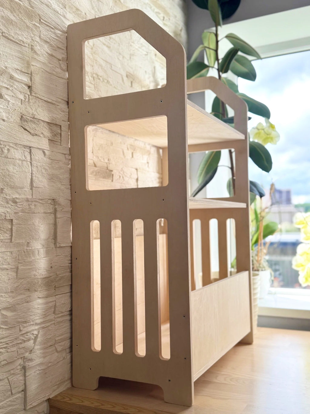 a bold, low-profile montessori shelf in natural birch, shown from a dramatic low angle to emphasize its accessible design for toddlers