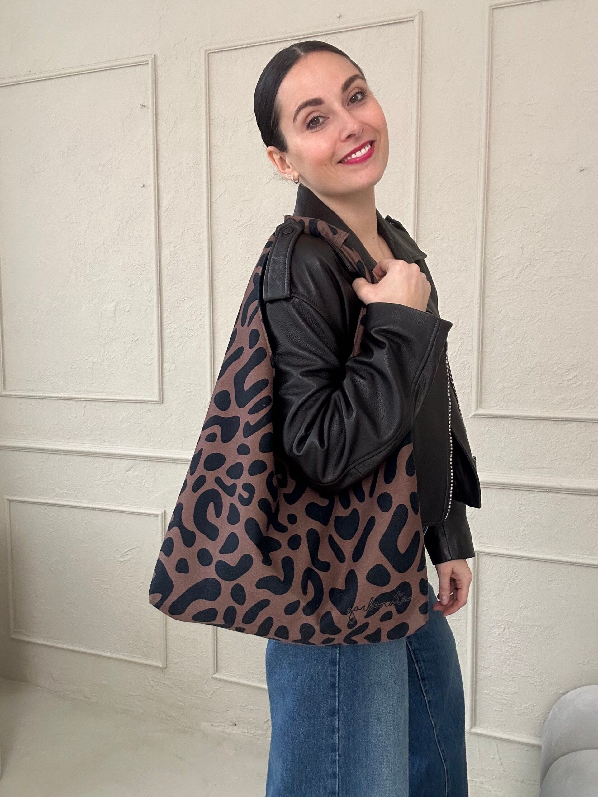 confident woman holding a bold leopard print moon bag against an urban backdrop