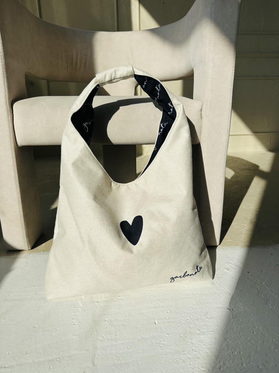 playful white moon bag heart held against a sunny backdrop, showing off its lightweight, fun shape