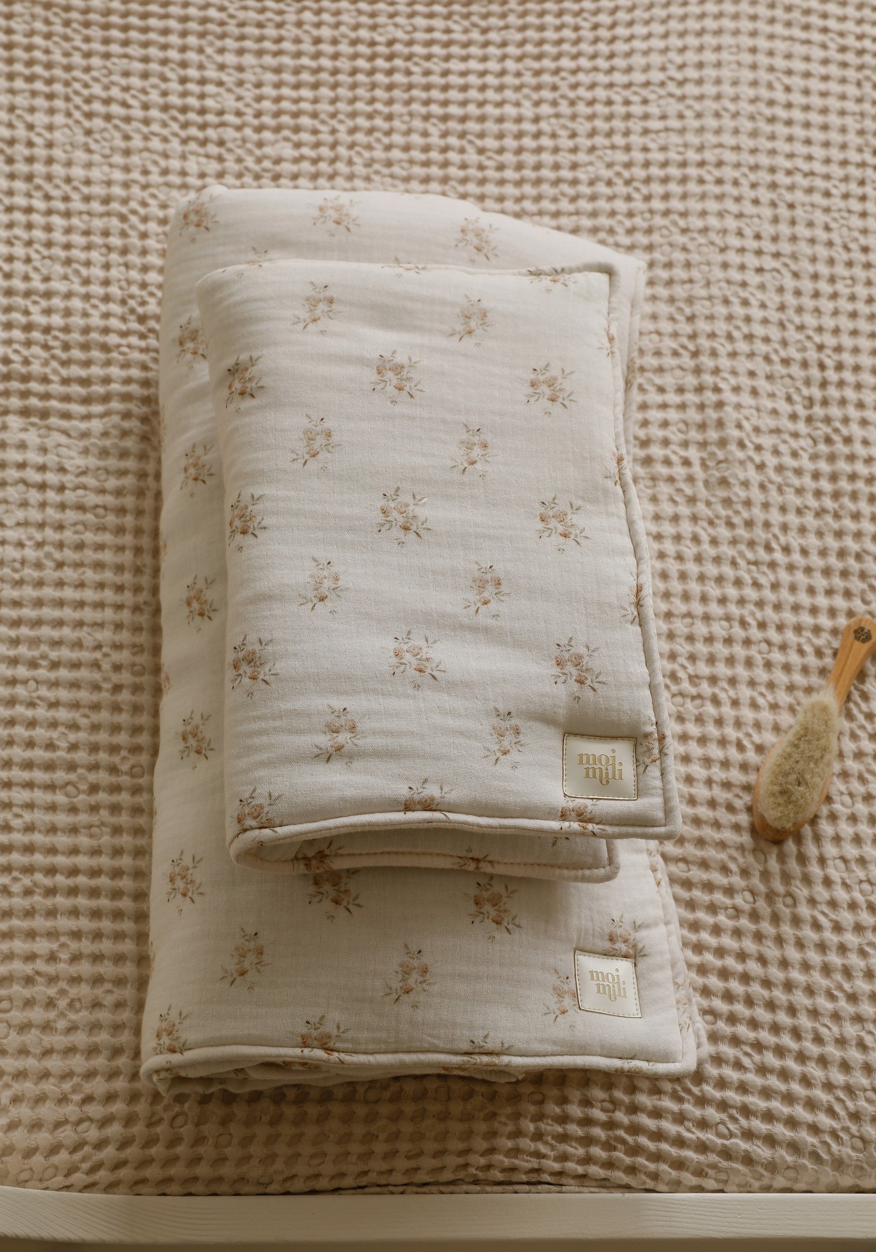 soft muslin baby blanket and pillow set with boho flowers, laid flat on a wooden surface for size reference