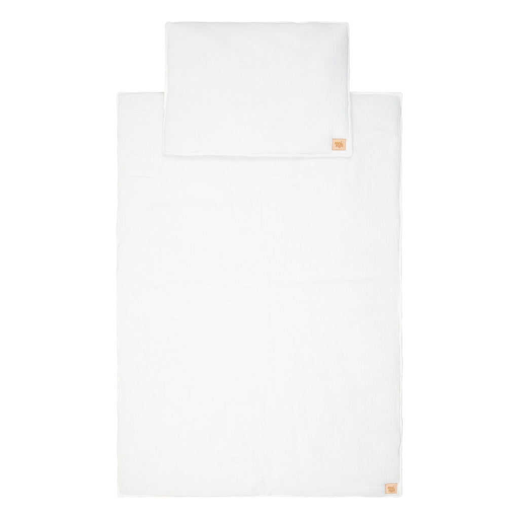 soft cream muslin baby blanket and pillow set draped gently over a cozy nursery chair