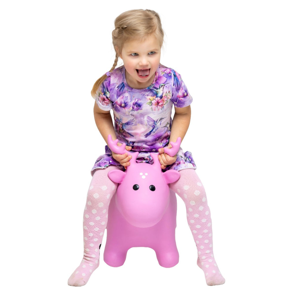 a toddler laughing while bouncing on a vibrant pink moose hopper toy indoors