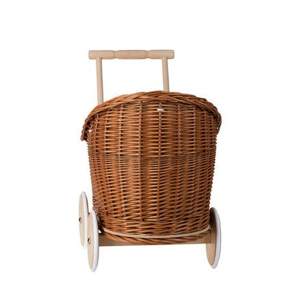 a child's hand gently tucking a doll into the natural wicker pram with soft beige bedding