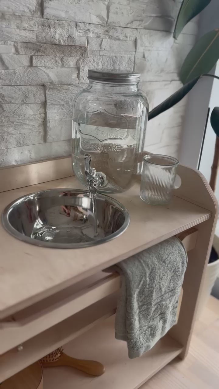 a child's wooden washbasin with enamel bowl and open shelf, shown in a bright, functional home setting