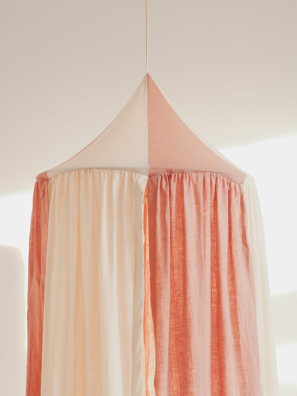 powder pink organic cotton canopy hanging in a sunlit garden nook with soft morning light