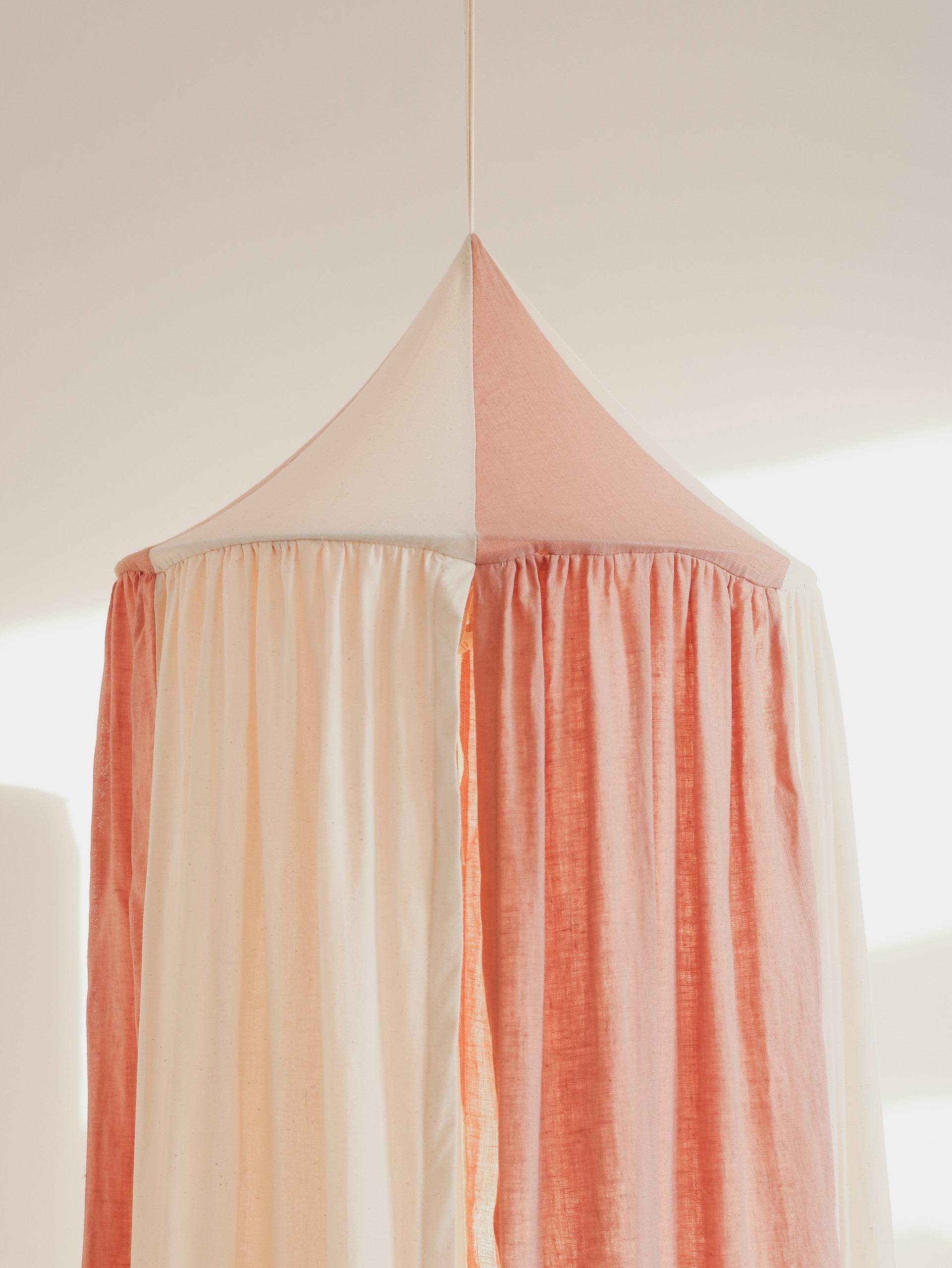 powder pink organic cotton canopy hanging in a sunlit garden nook with soft morning light