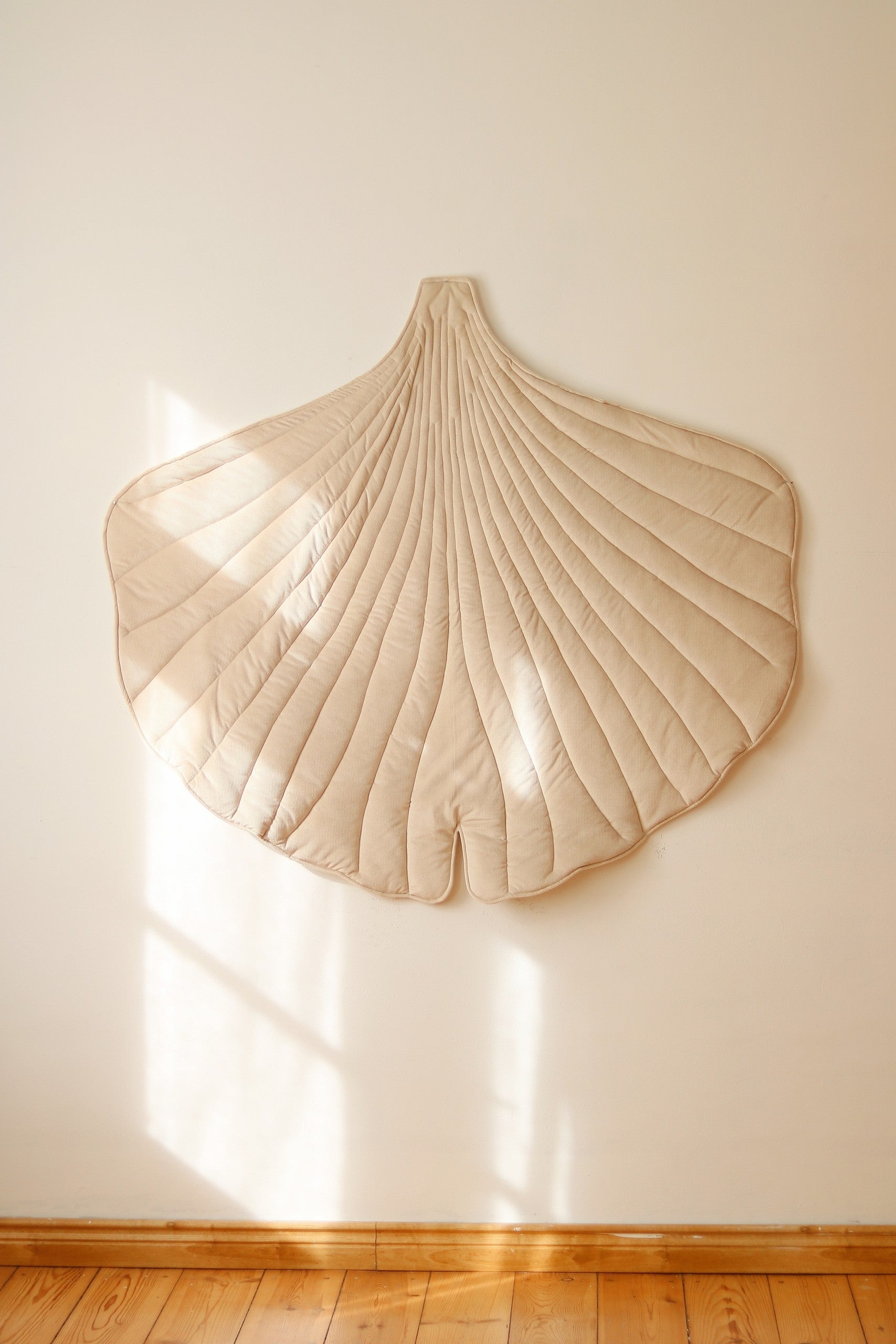 elegant cream ginkgo leaf playmat on a hardwood floor, showcasing its refined handmade texture