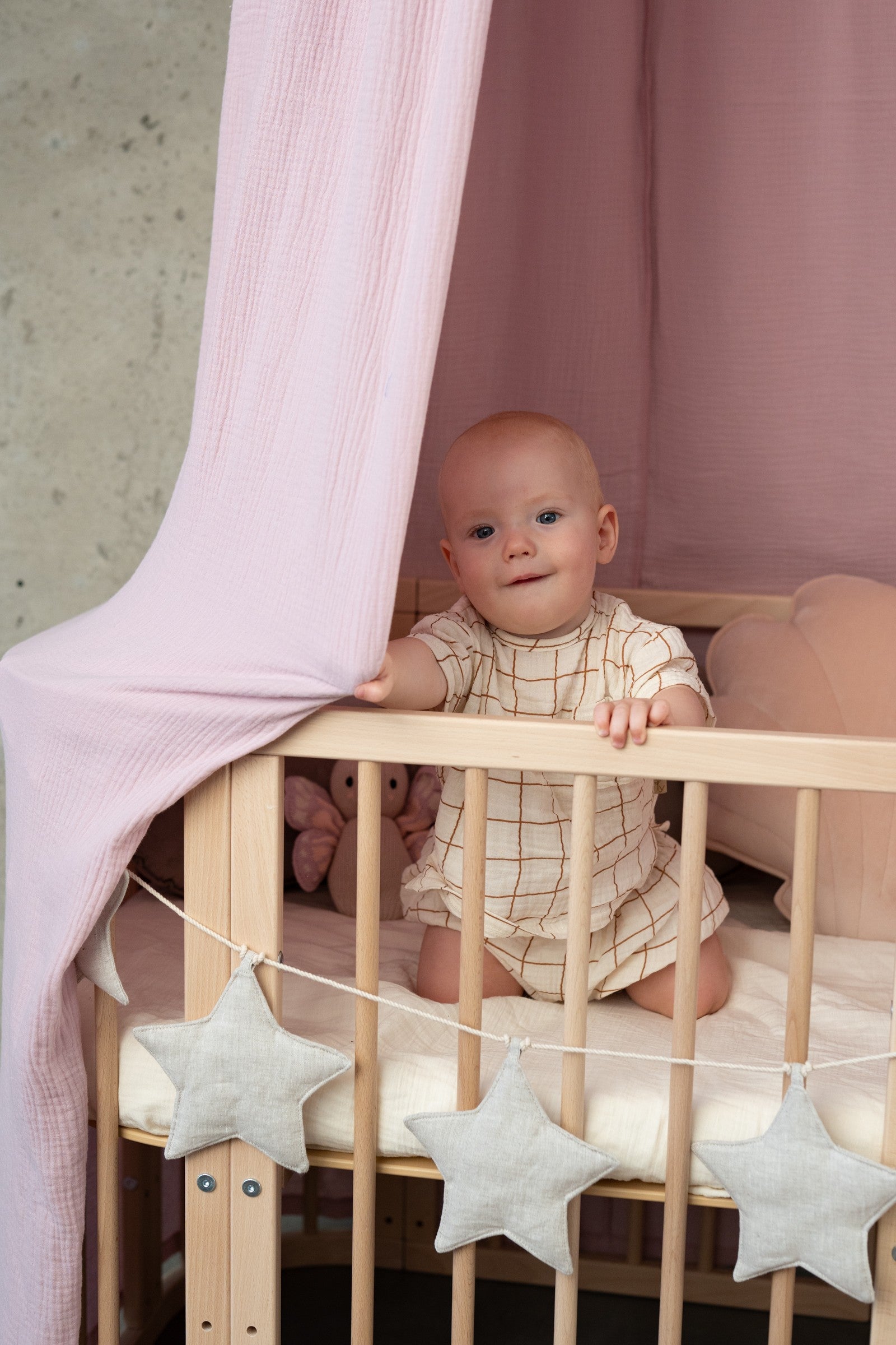 baby pink organic cotton canopy hanging over a cozy reading nook with soft lighting