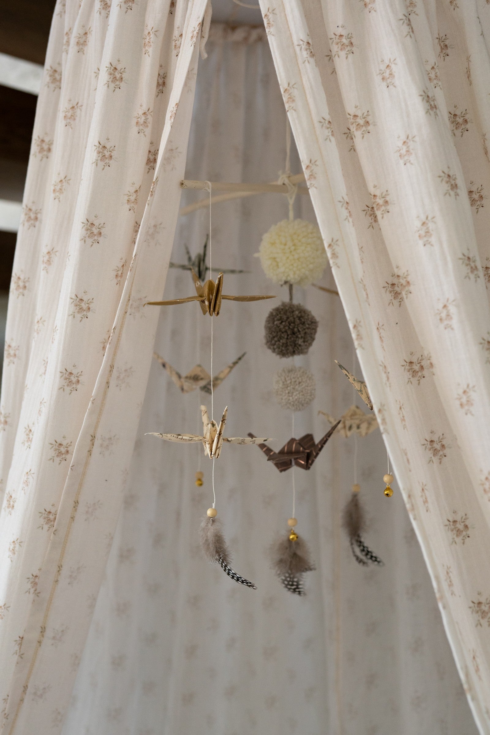 playful gold dust origami mobile with spinning cranes and pompoms above a crib, soft sunlight glow