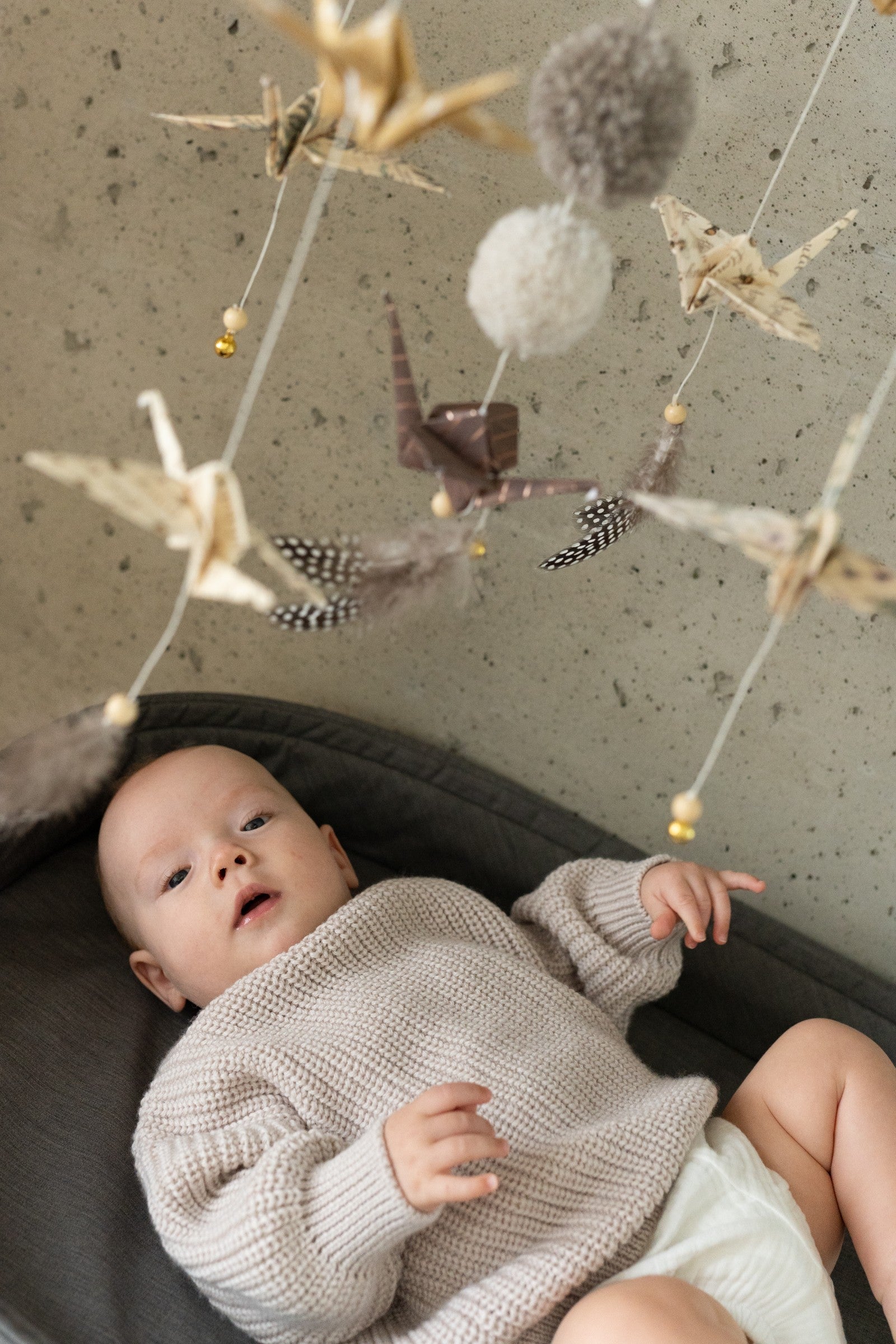 elegant gold dust origami nursery mobile with delicate paper cranes and pompoms, softly lit in a serene nursery