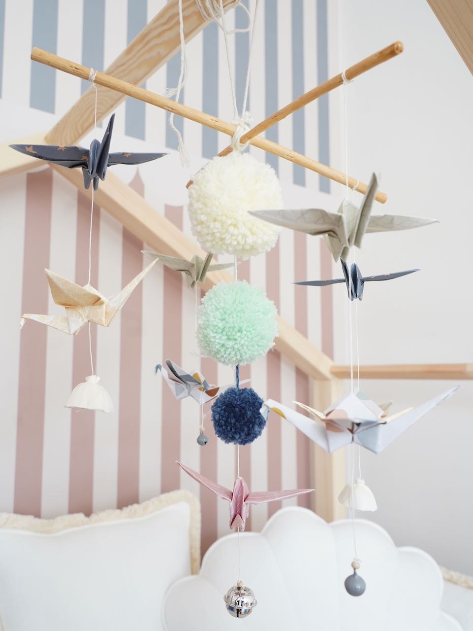 soft pastel origami nursery mobile with delicate paper cranes and pompoms, gently swaying above a crib