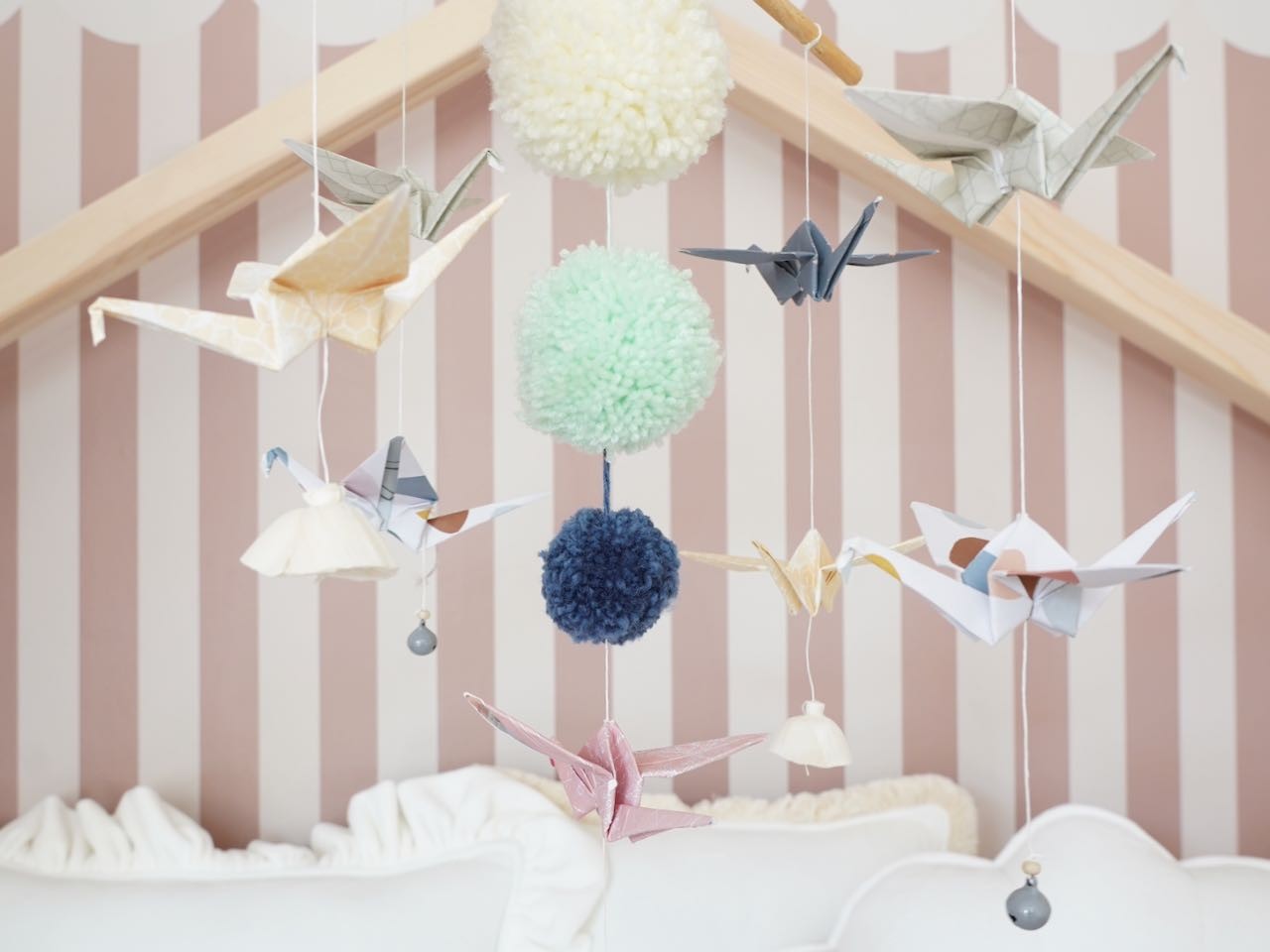 playful pastel origami nursery mobile with dangling cranes and pompoms, spinning gently above a crib