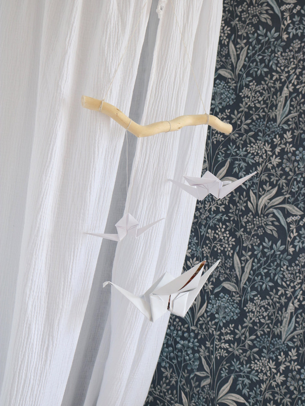 soft white origami crane mobile with yarn pompoms hanging gently over a crib