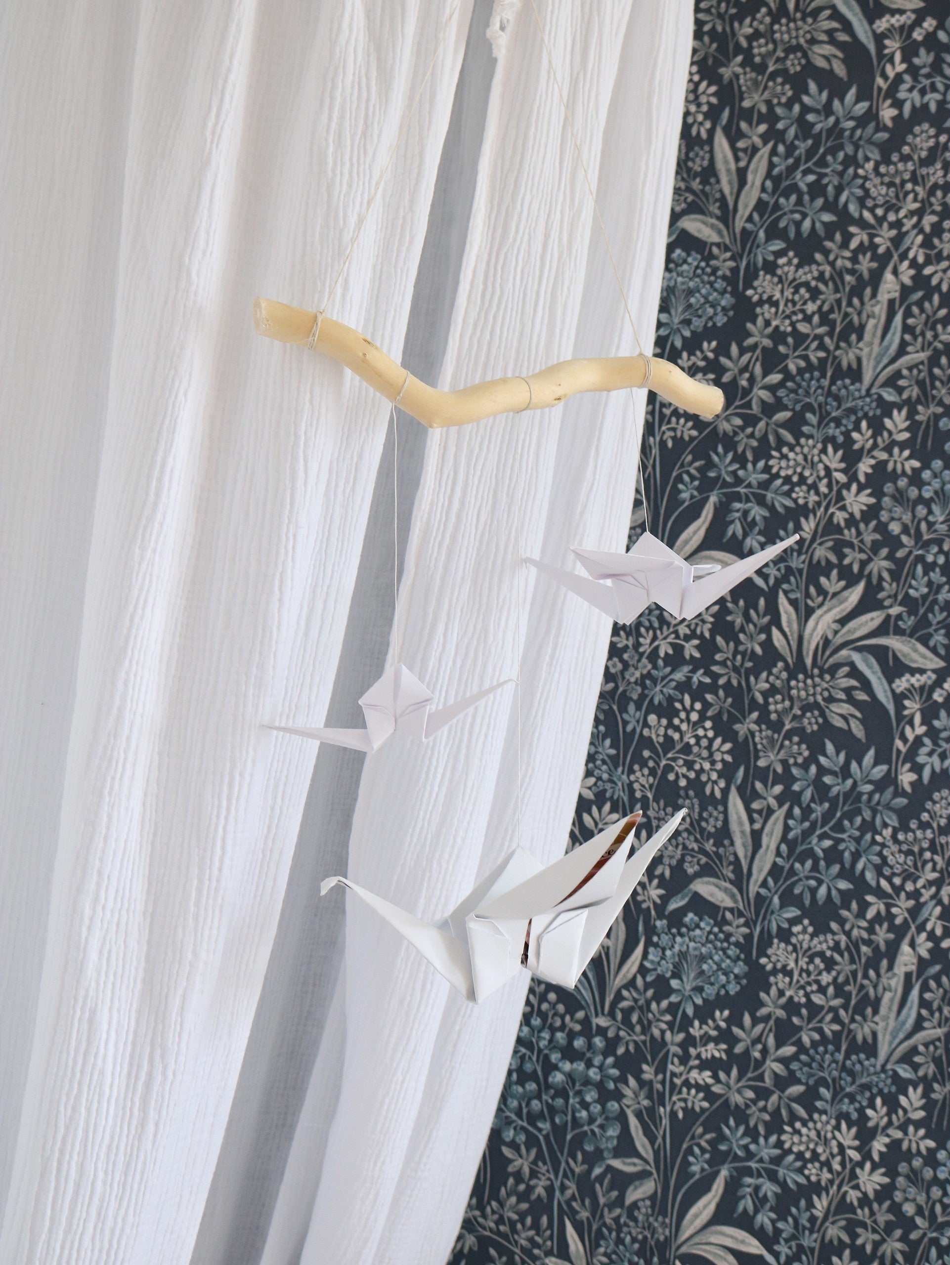 soft white origami crane mobile with yarn pompoms hanging gently over a crib