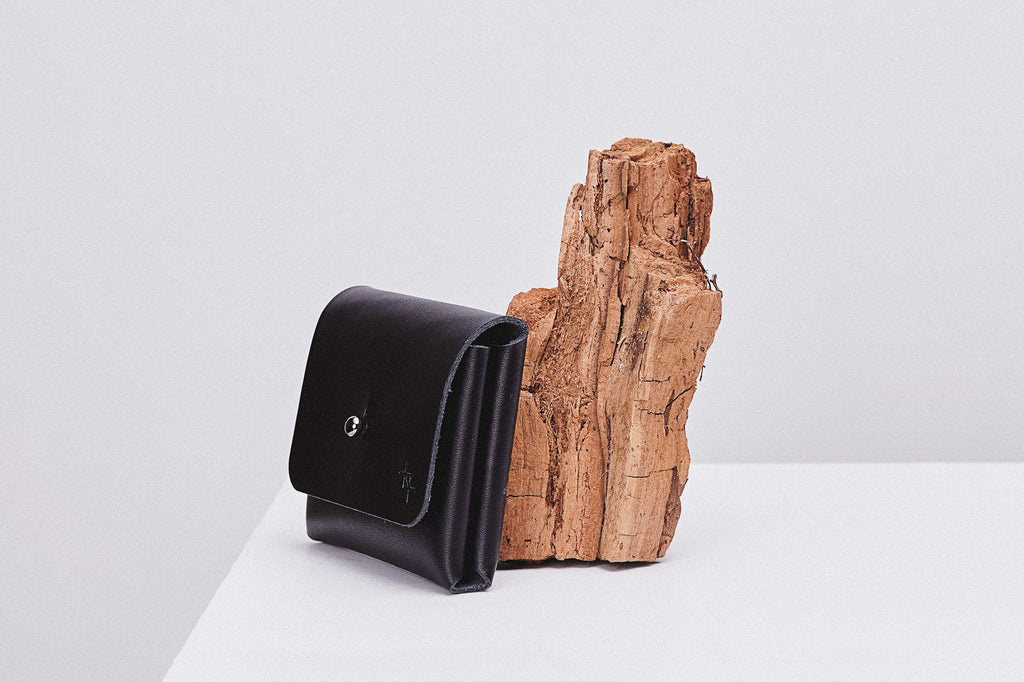 softly lit minimalist leather pouchie wallet with its adjustable strap resting on a cozy surface