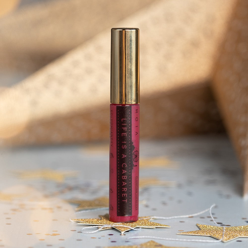 life is a cabaret plumping lip gloss with a bold, high-shine finish in dramatic lighting