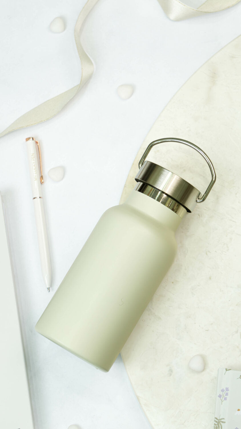 a soft beige water bottle held in a cozy hand, resting on a warm wooden table