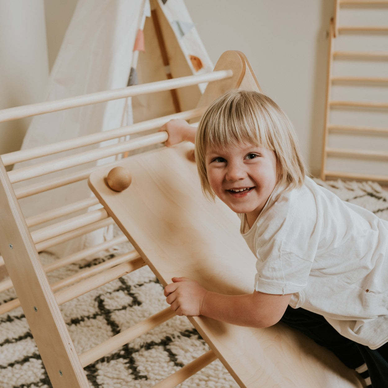 a soft-lit toddler testing the textured rock holds on the birch plywood climbing ramp