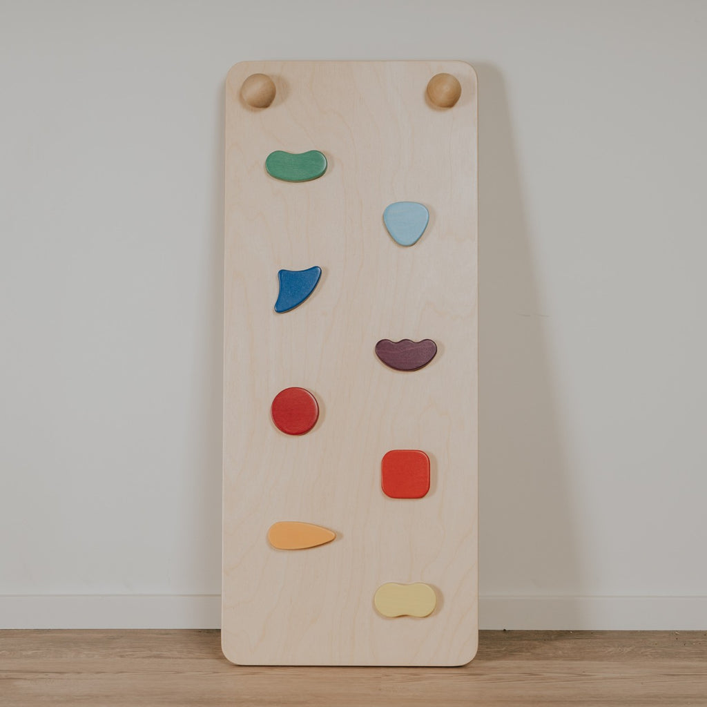 a child's hand gripping a rainbow ramp's rock hold in soft morning light