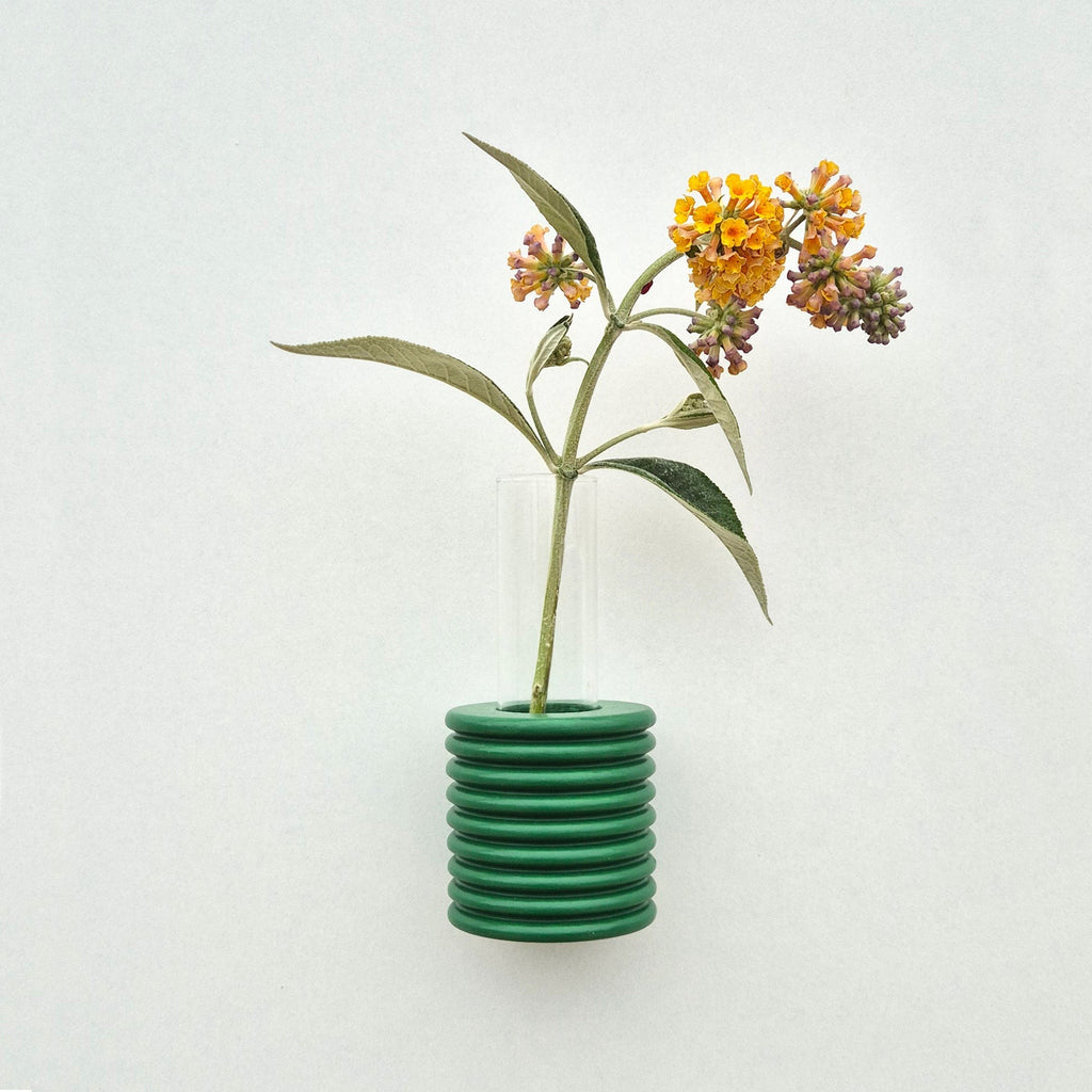 bold green ribble wall vase mounted on a bright white wall with a single fresh flower