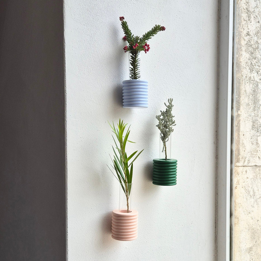green ribble wall vase mounted on a beige wall with a single dried flower