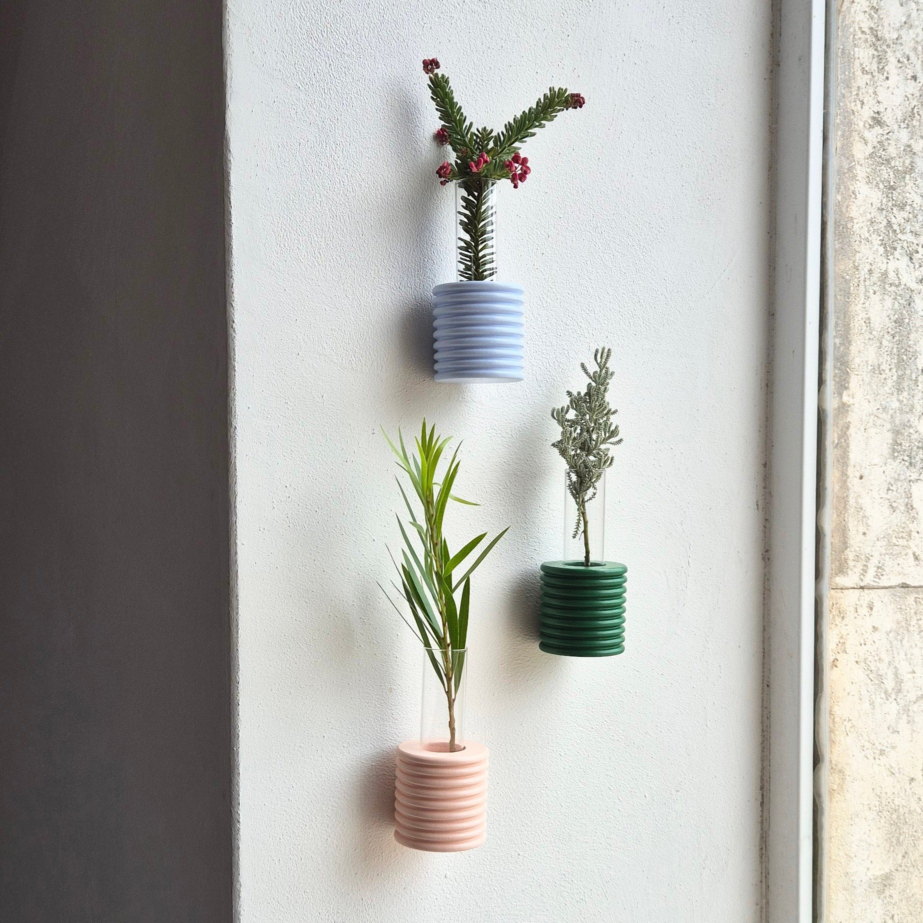 green ribble wall vase mounted on a beige wall with a single dried flower