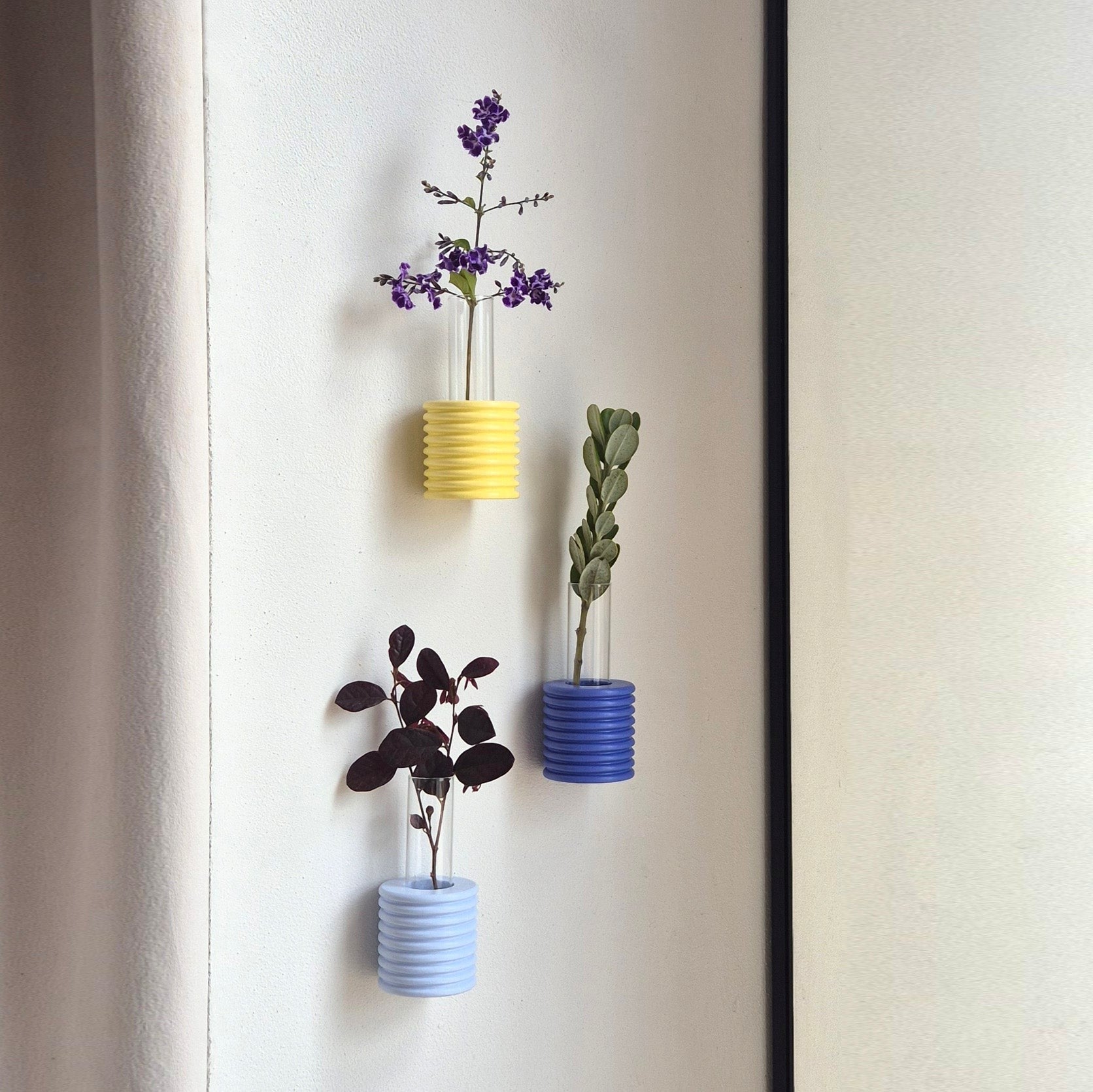 close-up of a blue ribble wall vase mounted on a beige wall with a single dried flower
