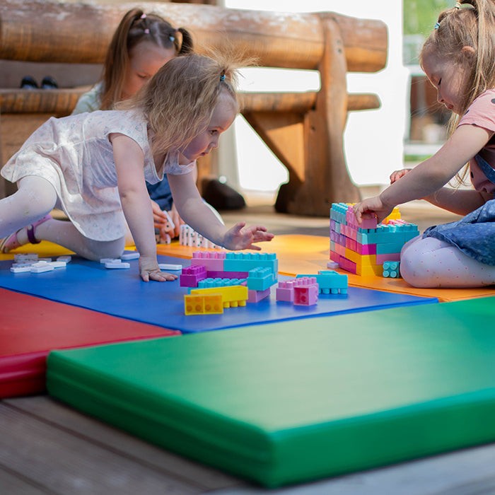 a toddler laughing while building a colorful igloo fort with soft foam play mats