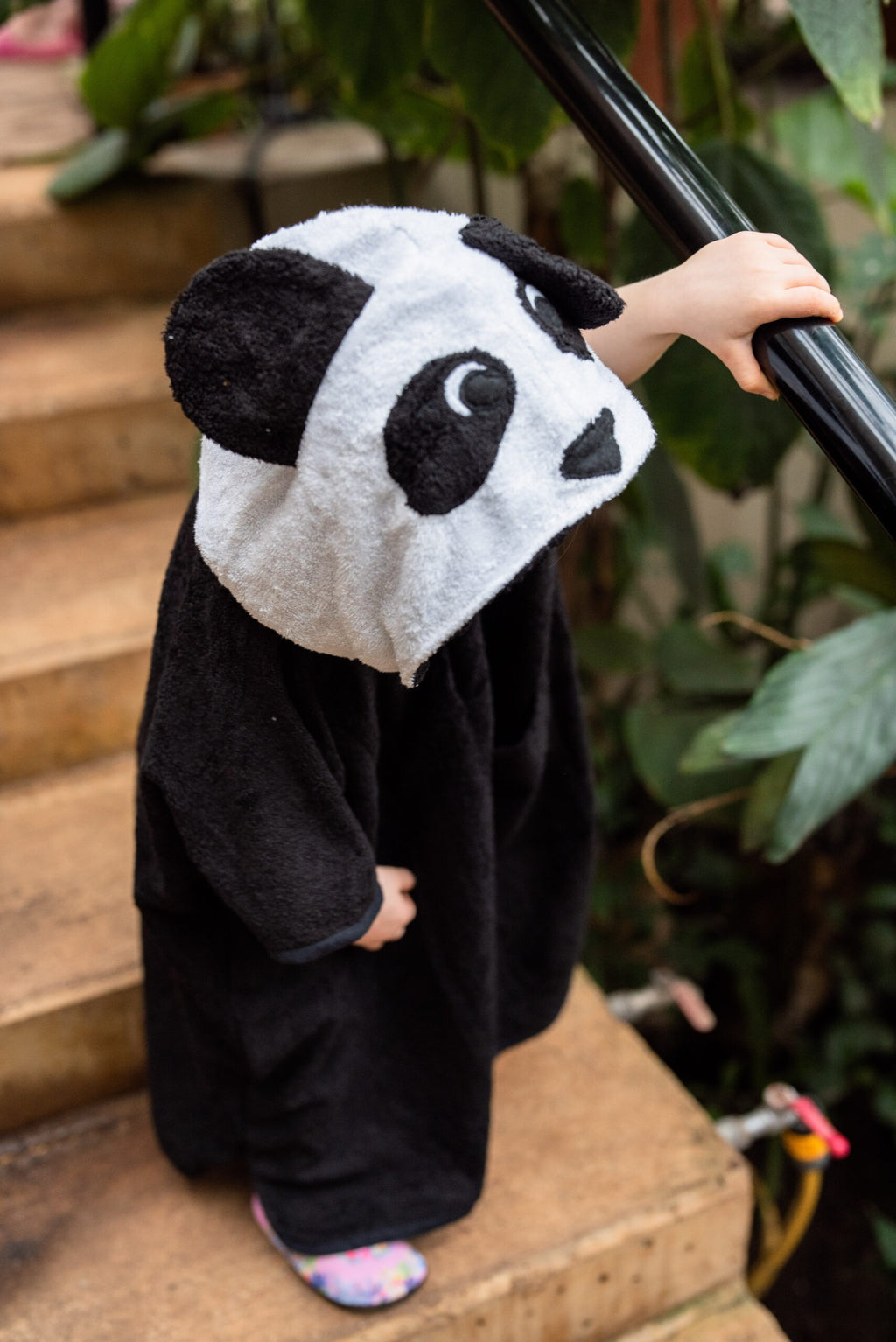 toddler in a soft bamboo panda poncho, side-lit and cozy, holding a small toy from its pocket