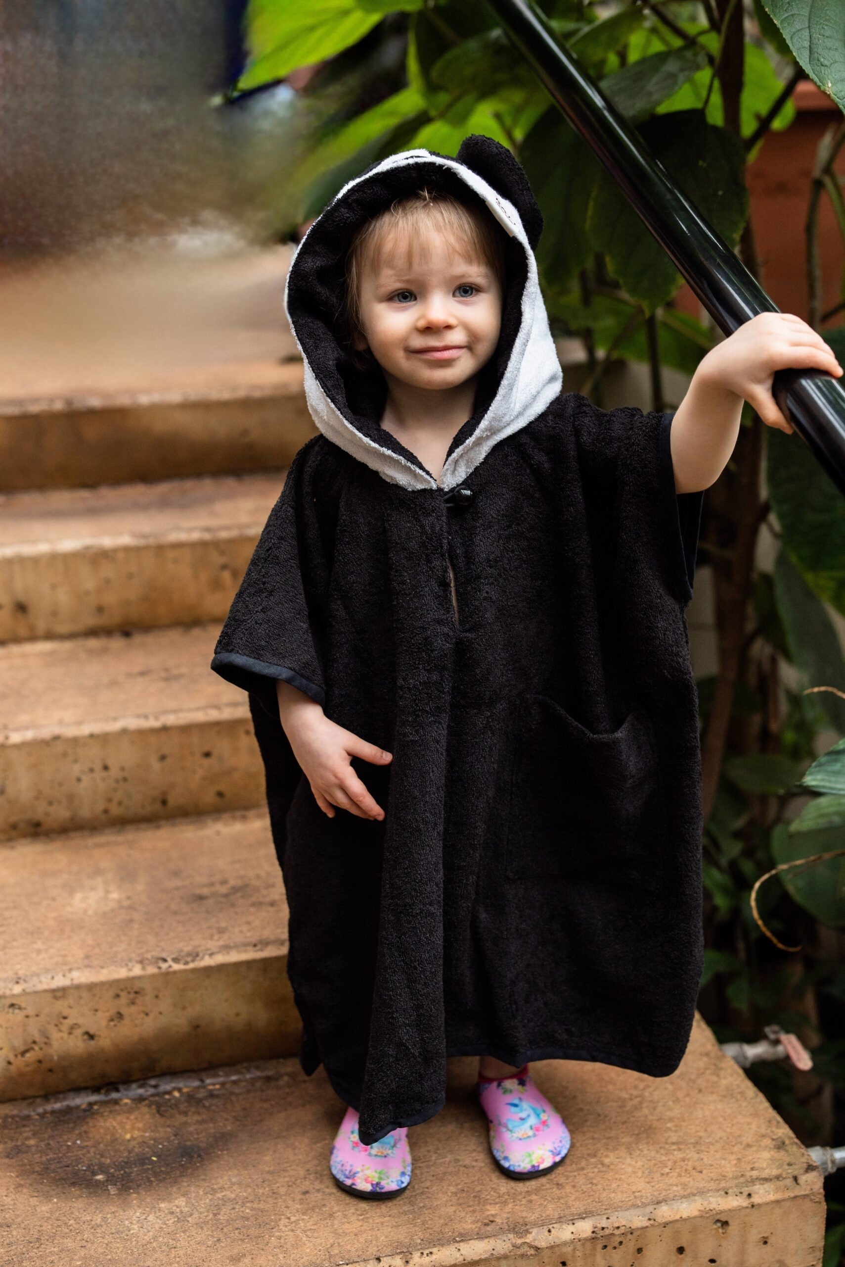 toddler in a playful panda poncho laughing, holding a toy from its pocket on a sunny beach