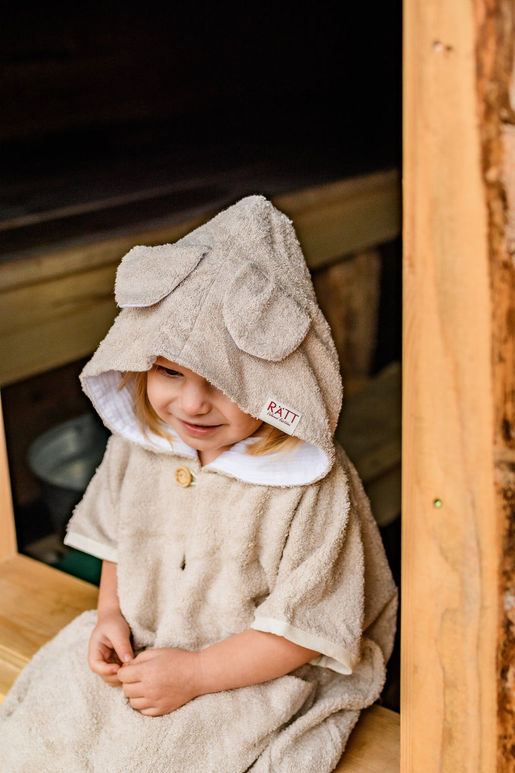 a giggling toddler in a soft bamboo poncho twirling, showing off the playful hood and handy pockets