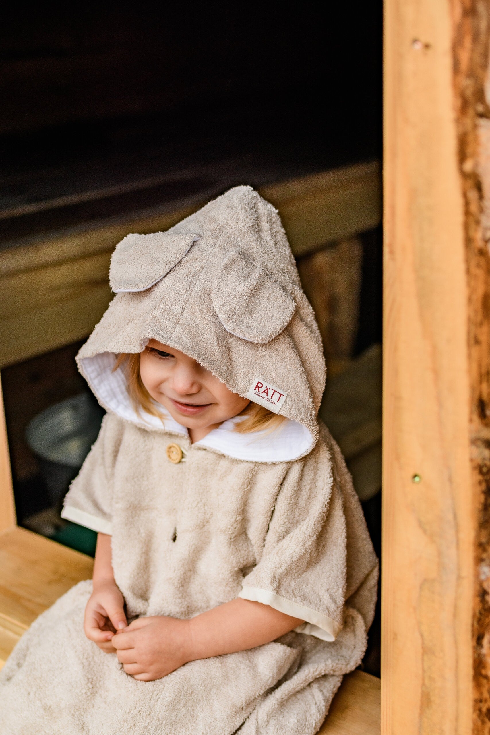 a giggling toddler in a soft bamboo poncho twirling, showing off the playful hood and handy pockets