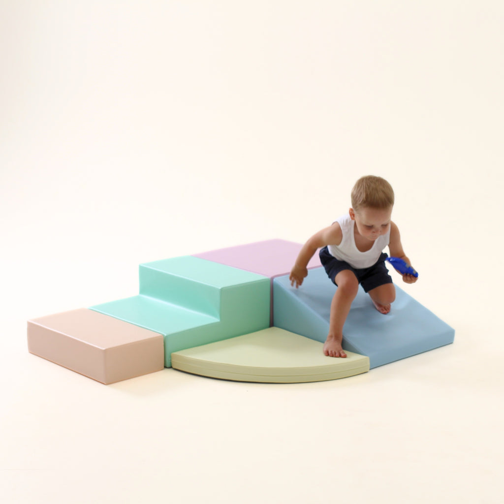 a child's hand reaching for the top of a soft pastel foam corner climber in a sunlit playroom