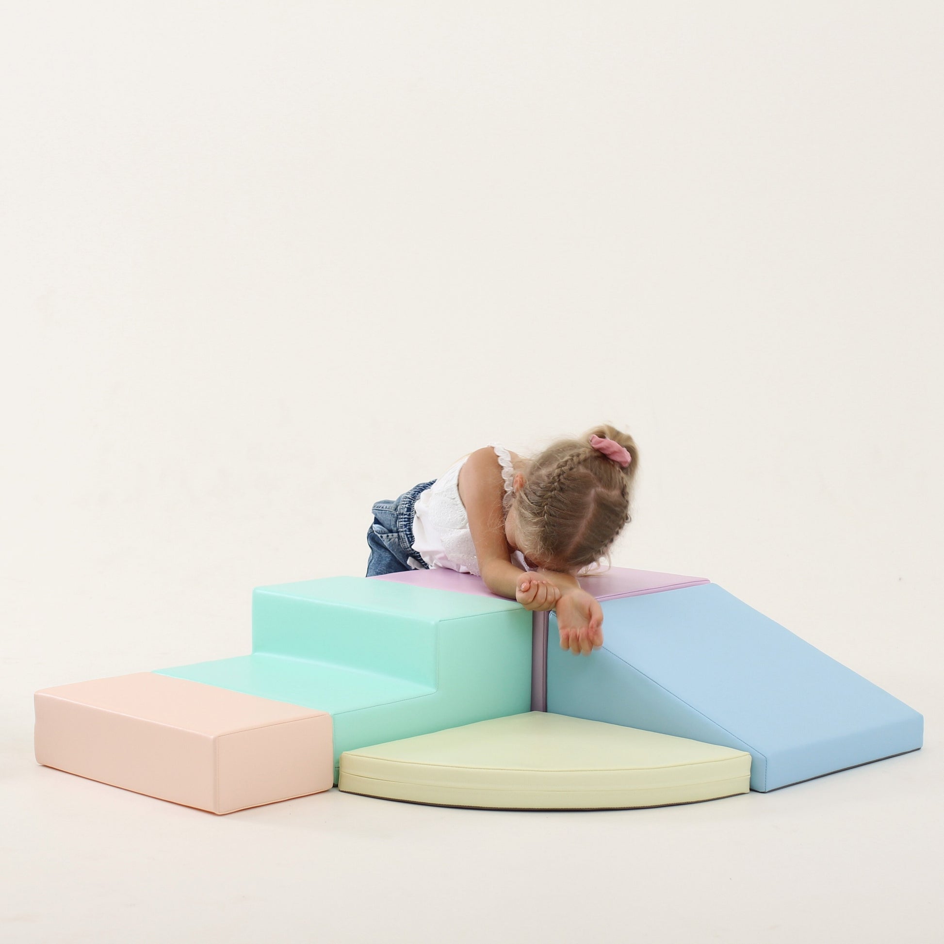 child climbing on a soft pastel foam corner climber in a sunlit playroom