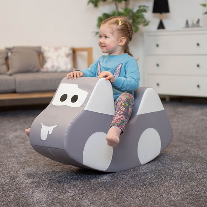 a soft grey plush ride-on car for toddlers, shown in a cozy nursery setting